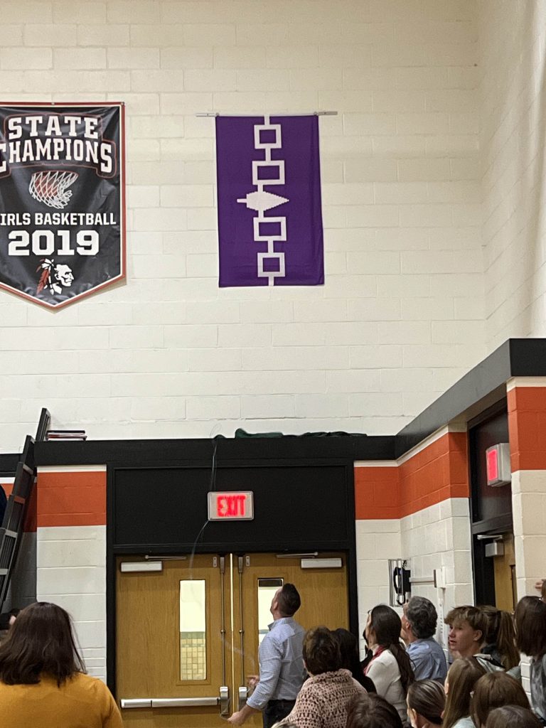 The flag mounted on the gym wall next to a state championship banner