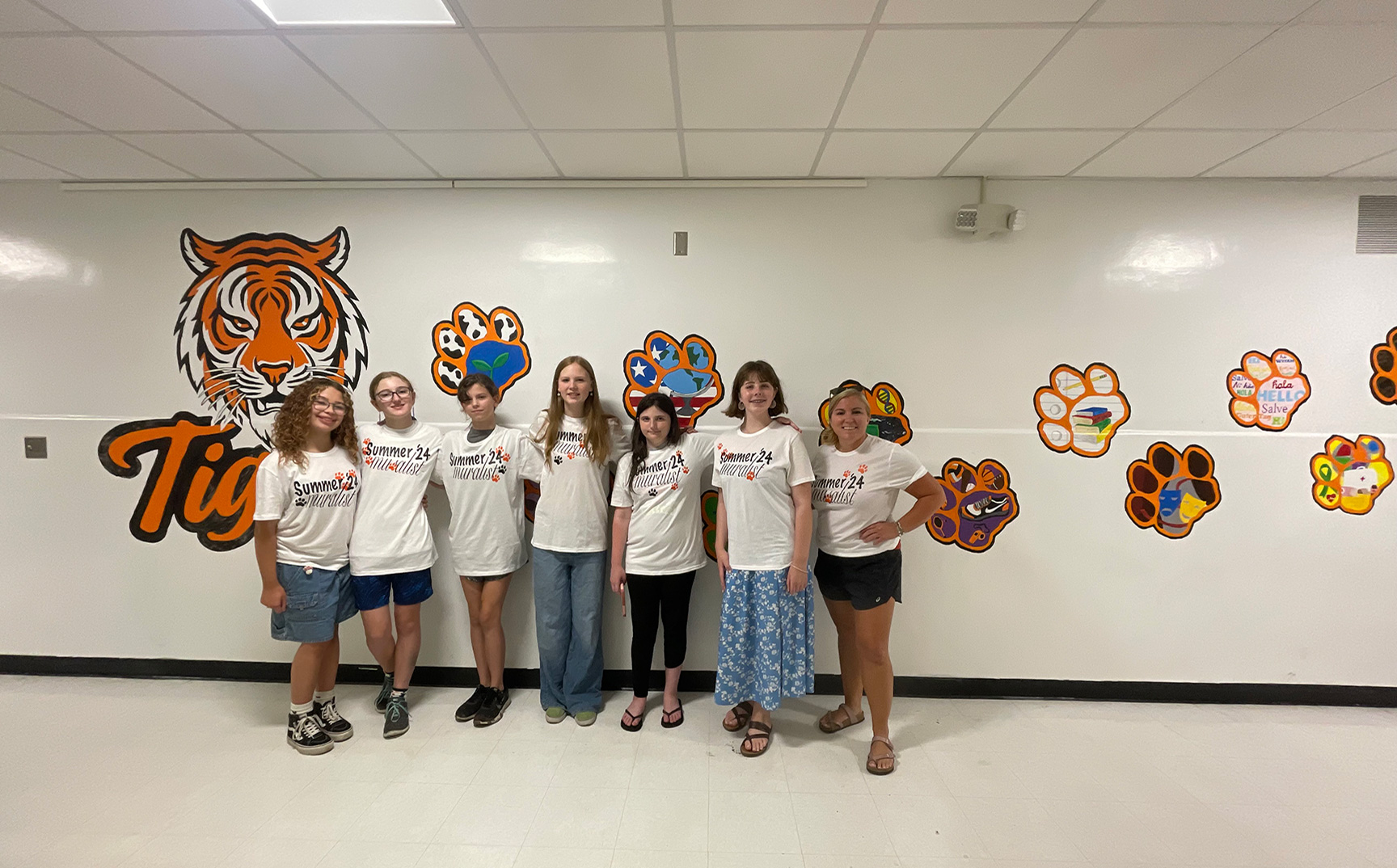 Students and HS art teacher Ms. O'Brien standing in front of a Tiger mural